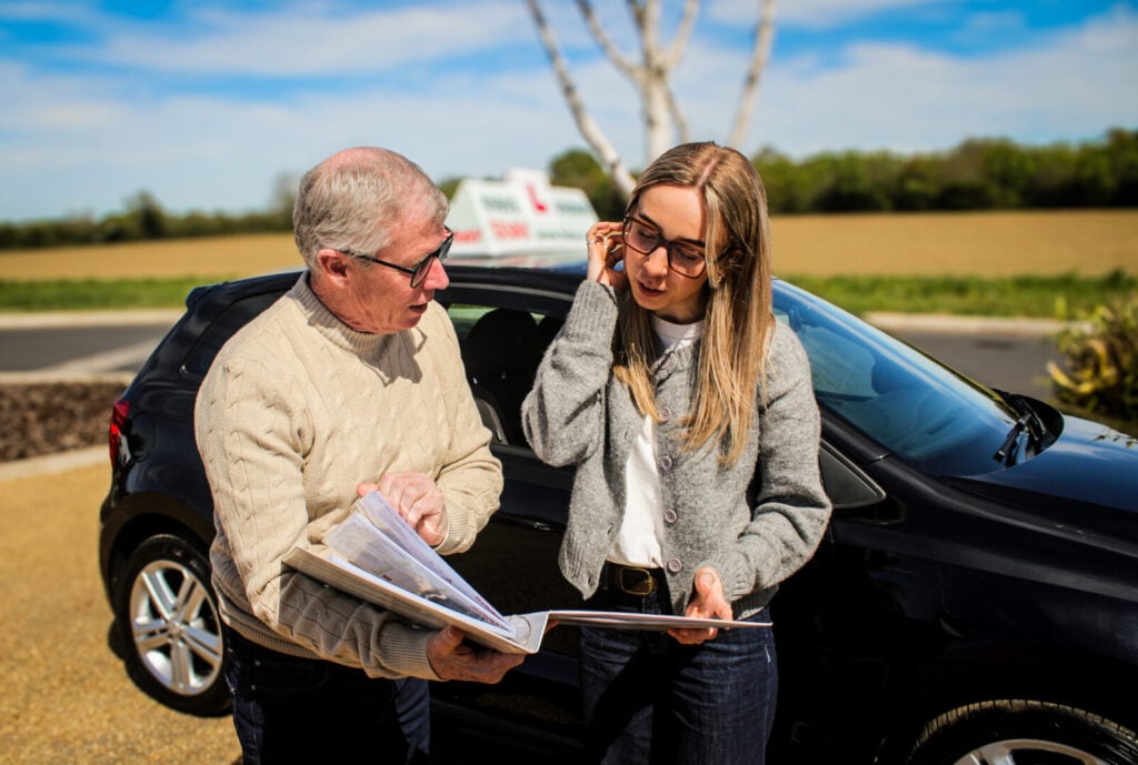 Driving instructor and learner driver discussion driving theory next to a 5day vehicle